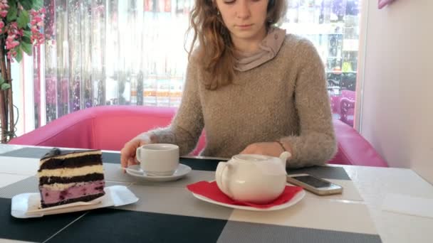 Primer plano mano femenina acariciando la taza de té en la cafetería. Mujer en restaurante con bebida caliente y pastel — Vídeo de stock