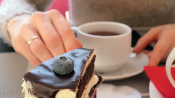 Primer plano mano femenina acariciando la taza de té en la cafetería. Mujer en restaurante con bebida caliente y pastel — Vídeos de Stock