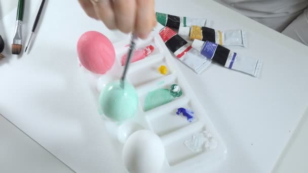 Женщина рисует пасхальные яйца цветными красками крупным планом — стоковое видео