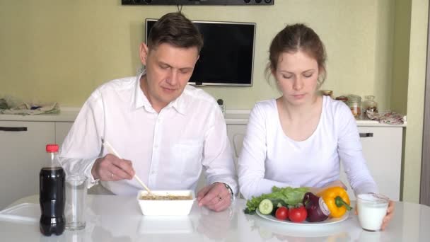 Una esposa y un marido están sentados en una mesa comiendo fideos chinos y verduras frescas. El concepto de nutrición adecuada y estilo de vida saludable — Vídeos de Stock