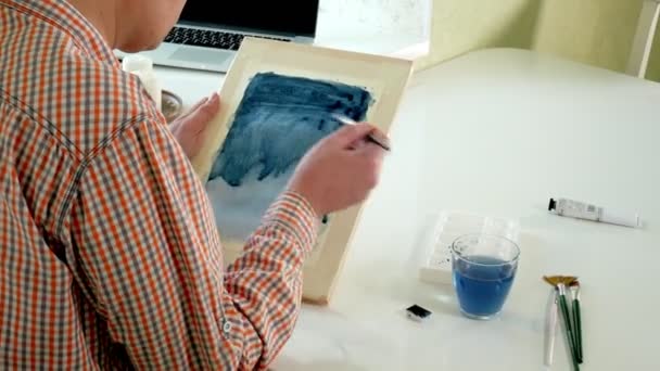 Дорослий чоловік малює кольоровими акварельними фарбами в домашній студії — стокове відео