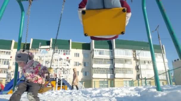 Madre joven con el niño balanceándose en el columpio al aire libre en el parque de invierno. Caída de nieve, nevadas, invierno — Vídeos de Stock