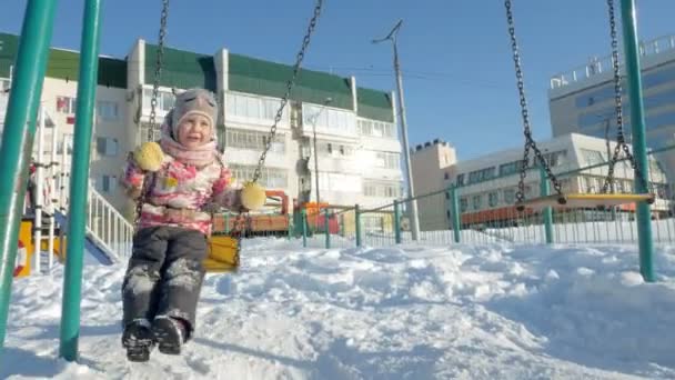 Молодая мама с ребенком качается на качелях на открытом воздухе в зимнем парке. Снегопад, снегопад, зимнее время — стоковое видео