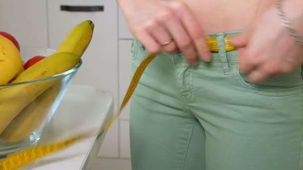 Тонкая женщина измеряет талию на фоне тарелки с фруктами и овощами, здоровый образ жизни — стоковое видео