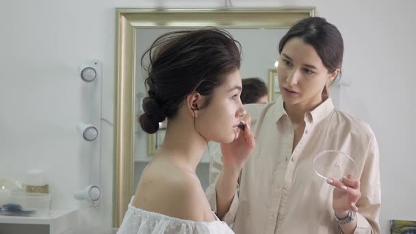 Jeune belle femme appliquant maquillage par maquilleuse — Video