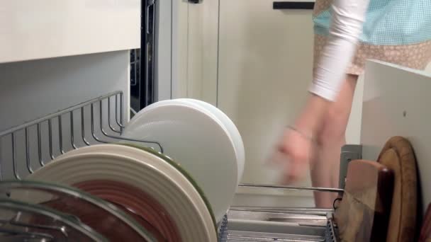 En ung kvinna lägger en ren maträtt från diskmaskin — Stockvideo