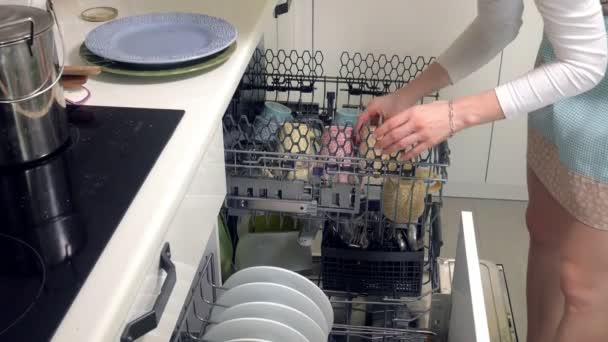 Молодая женщина кладет чистую тарелку из посудомоечной машины — стоковое видео