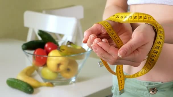 Тонкая женщина держит меру на фоне тарелки с фруктами и овощами, здоровый образ жизни — стоковое видео