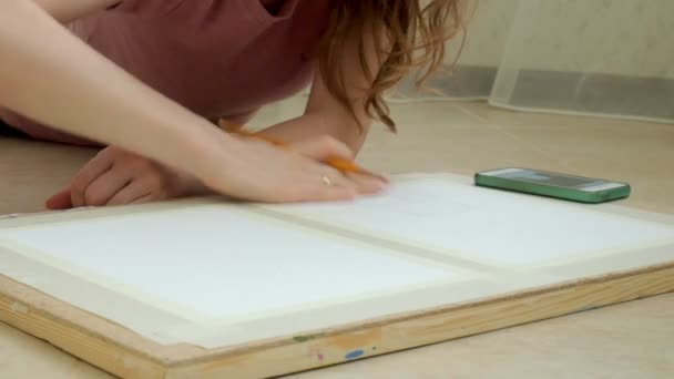 Mujer joven tendida en el suelo y dibuja un lápiz en la tableta — Vídeos de Stock