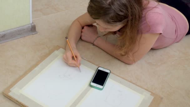 Mujer joven tendida en el suelo y dibuja un lápiz en la tableta — Vídeos de Stock