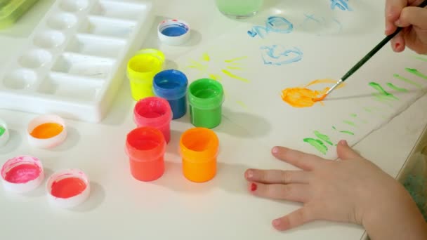 Krásná zrzavá holčička maluje štětcem paintand sedí u stolu — Stock video