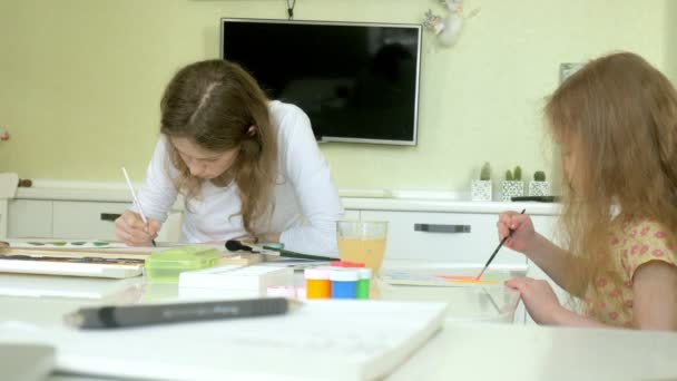 Little beautiful red-haired girl and mother paints with paintand brush sitting at table — Stock Video