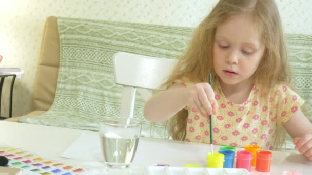 Kleine schöne rothaarige Mädchen malt mit Farbe und Pinsel am Tisch sitzend — Stockvideo