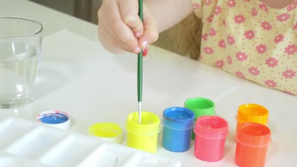 Little beautiful red-haired girl paints with paintand brush sitting at table — Stock Video