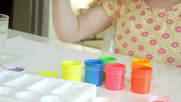 Little beautiful red-haired girl paints with paintand brush sitting at table — Stock Video