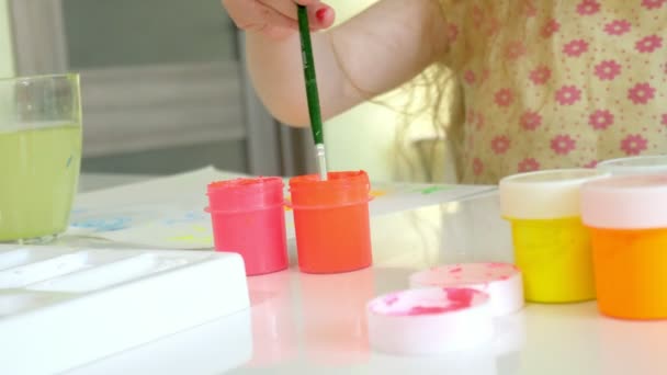 Krásná zrzavá holčička maluje štětcem paintand sedí u stolu — Stock video