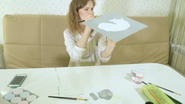 Маленька красива руда жінка малює фарбою і пензлем, сидячи за столом — стокове відео