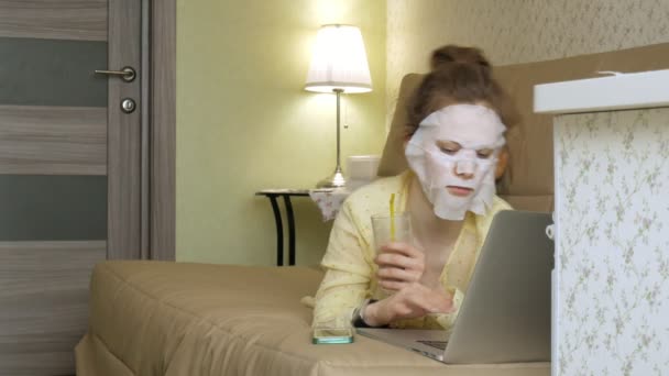 Jovem mulher fazendo máscara facial com máscara de limpeza, trabalhando atrás do laptop em casa — Vídeo de Stock