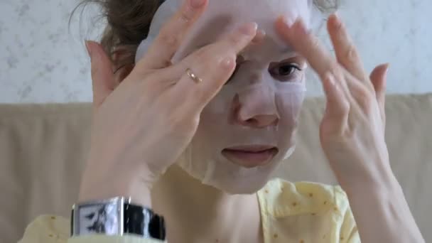 Jonge vrouw doet facial mask masker met zuivering masker op gezicht in keuken thuis — Stockvideo