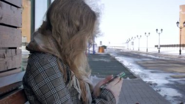 Akıllı telefon kullanan kadın güzel parkta bankta rahatlatır. Telefonun ekranına jestleri yapımında genç kadın. Teknoloji açık havada