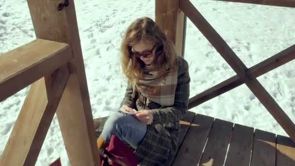 A young woman sits on a wooden veranda, silently touching the origami paper plane with her fingers and putting it on her knees. Girl sitting outdoors with white aerogamy aircraft, close view, — Stock Video