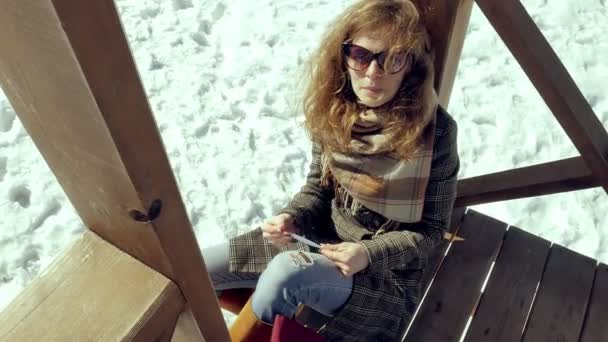 Una giovane donna si siede su una veranda di legno, toccando silenziosamente l'aereo di carta origami con le dita e mettendolo in ginocchio. Ragazza seduta all'aperto con aereo aerogamia bianco, vista da vicino , — Video Stock