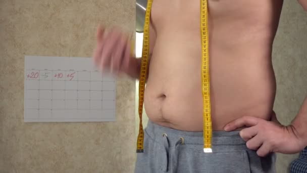 Толстяк измеряет свою талию, большой пивной живот, здоровый образ жизни, поедающий яблоко — стоковое видео