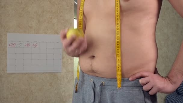 Een dikke man maatregelen zijn taille, een grote bierbuik, een gezonde levensstijl het eten van een appel — Stockvideo