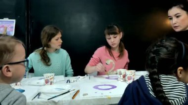 Çocuk erkek ve kız birlikte sınıf ve çizim masasının etrafında oturuyor. Onlarla birlikte onların genç ve güzel bir öğretmendir.