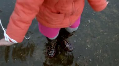 Küçük güzel kız su birikintileri üzerinde yağmur sonrası atlama