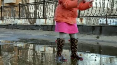Küçük güzel kız su birikintileri üzerinde yağmur sonrası atlama