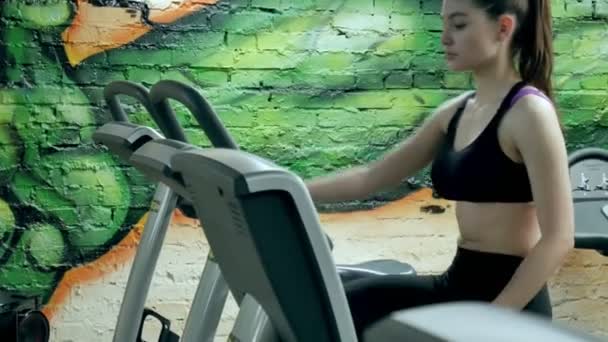 Jonge aantrekkelijke vrouw verbeteren haar uithoudingsvermogen tijdens het werken op een exercycle. Portret van een mooi meisje in de sportschool op een hometrainer. jonge vrouw op oefening fiets aërobe oefening — Stockvideo