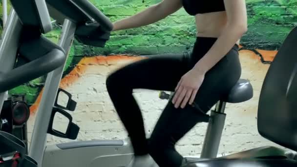 Jovem mulher atraente aumentando sua resistência durante o exercício em um ciclo de esforço. retrato de uma menina bonita no ginásio em uma bicicleta estacionária. jovem em bicicleta de exercício exercício aeróbico — Vídeo de Stock