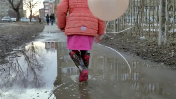 Маленька красива дівчинка стрибає на калюжах після дощу — стокове відео