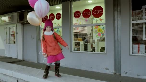 Ein kleines Mädchen spaziert mit bunten Luftballons auf einer Straße in der Stadt im zeitigen Frühling — Stockvideo