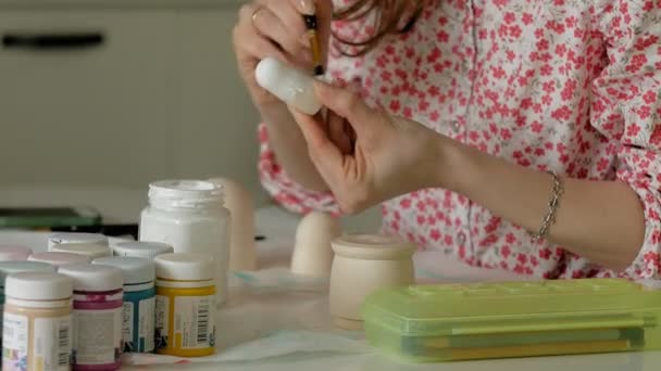 Uma mulher pinta uma boneca de madeira com tintas coloridas em seu estúdio em casa, pintura Matrioska — Vídeo de Stock