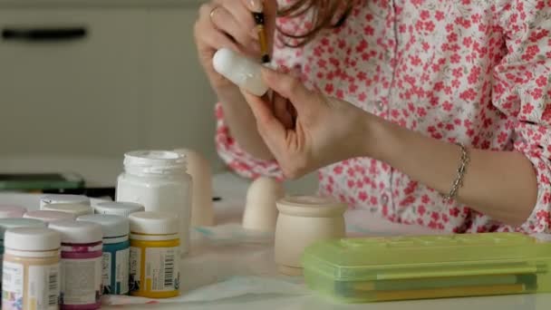 Une femme peint une poupée en bois avec des peintures colorées dans son studio à la maison, peinture Matryoshka — Video