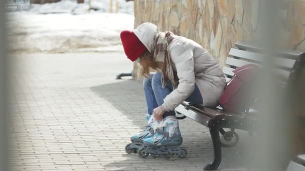 Fiatal gyönyörű nő sportos meleg ruhát és a görgők, ül egy fapadon, és készül a korcsolyázás ruhák görkorcsolya — Stock videók