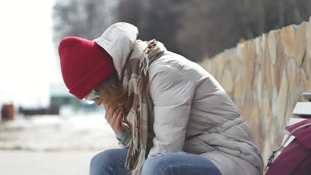 Young beautiful woman in sporty warm clothes and rollers, sitting on a wooden bench and dresses roller skates getting ready with skating — Stock Video