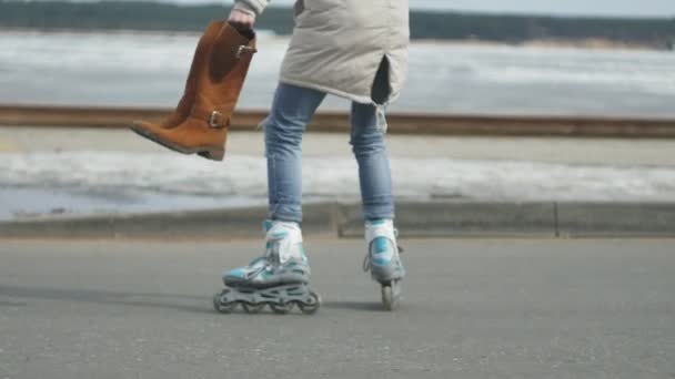 Young beautiful woman in a red hat, wearing sporty warm clothes and rollers, riding on the road on the coast — Stock Video