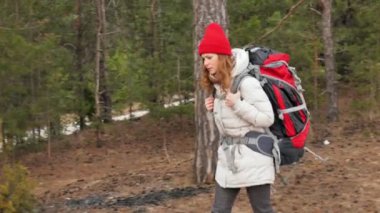 Çekici bir genç kadın kırmızı şapkalı bir büyük turistik sırt çantası ile erken baharda ormanda yürür