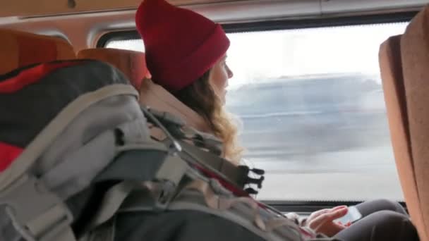 Giovane donna allegra con un cappello rosso, che viaggia in autobus in un giorno triste. Lei scatta foto su uno smartphone — Video Stock