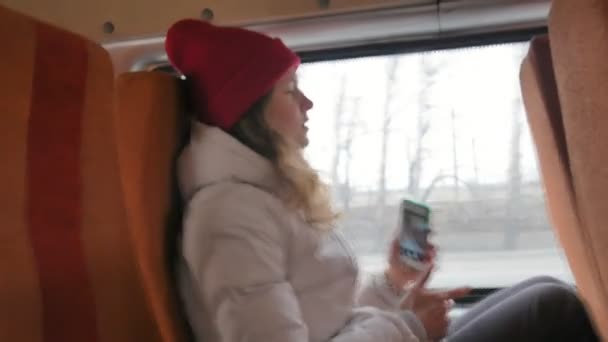 Μικρά χαρούμενα γυναίκα σε ένα κόκκινο καπέλο, ταξιδεύοντας με το λεωφορείο σε μια θλιβερή ημέρα. Παίρνει εικόνες σε ένα smartphone — Αρχείο Βίντεο