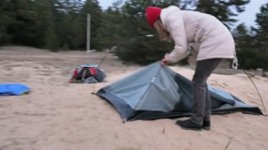 Çekici genç turist kadın kırmızı şapkalı bir turist çadır forest yakınındaki sahil üzerinde toplar.