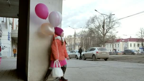 Маленька дівчинка гуляє з різнокольоровими кульками, на вулиці в місті ранньою весною — стокове відео