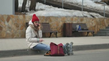 Kırmızı bir şapka giyen sportif sıcak giysiler ve Silindirler, asfalt yol üzerinde oturan ve telefonda konuşurken genç güzel kadın