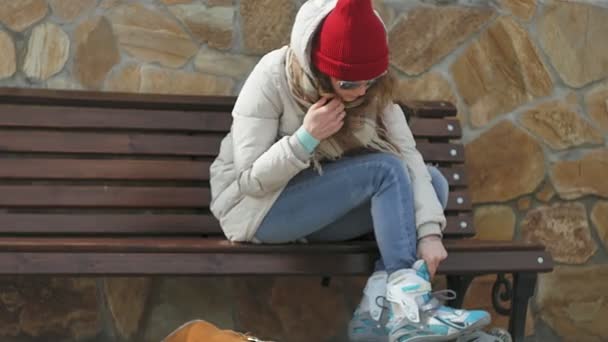 Sportif sıcak giysiler ve Silindirler, bir ahşap Bank ve elbiseler paten buz pateni ile hazırlanıyor oturan genç güzel kadın — Stok video