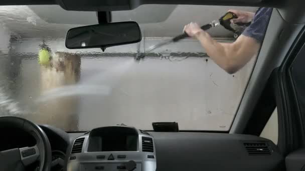 Автомобиль, проходящий через автомойку, человек моет машину бесконтактной раковиной, вид изнутри автомобиля — стоковое видео