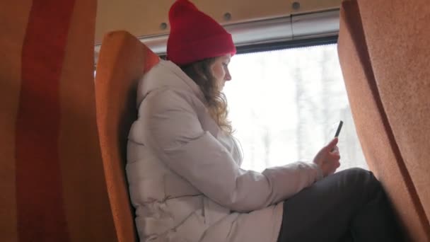 Jeune femme joyeuse avec un chapeau rouge, voyageant en bus un jour triste. Elle prend des photos sur un smartphone — Video