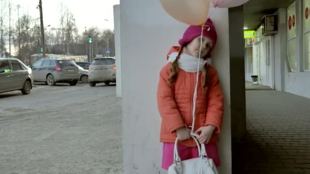 En liten flicka promenad med färgglada ballonger, på en gata i staden tidigt på våren — Stockvideo